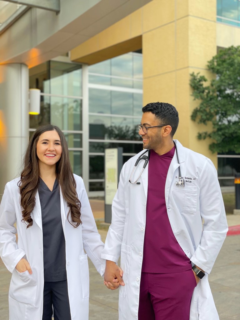 Dr. Nicolet and Dr. Joshua  holding hands and smiling in their white coats.